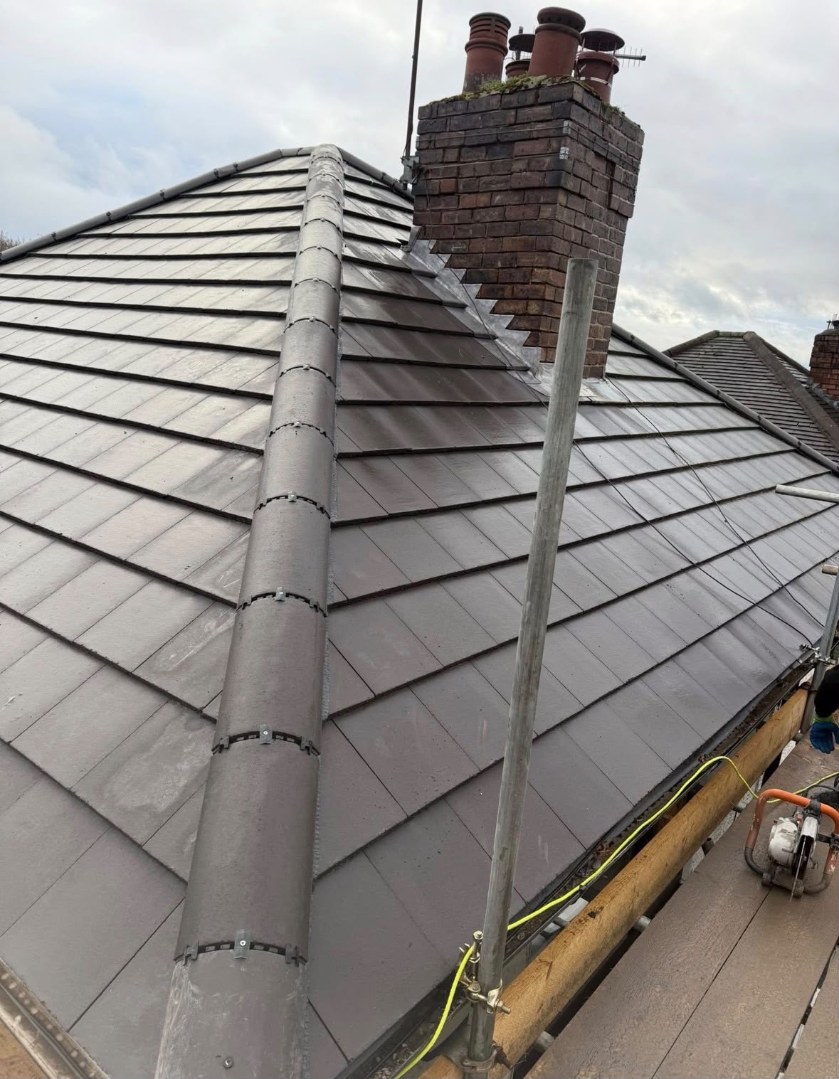 Grey roof tiles and ridge beside a brick chimney