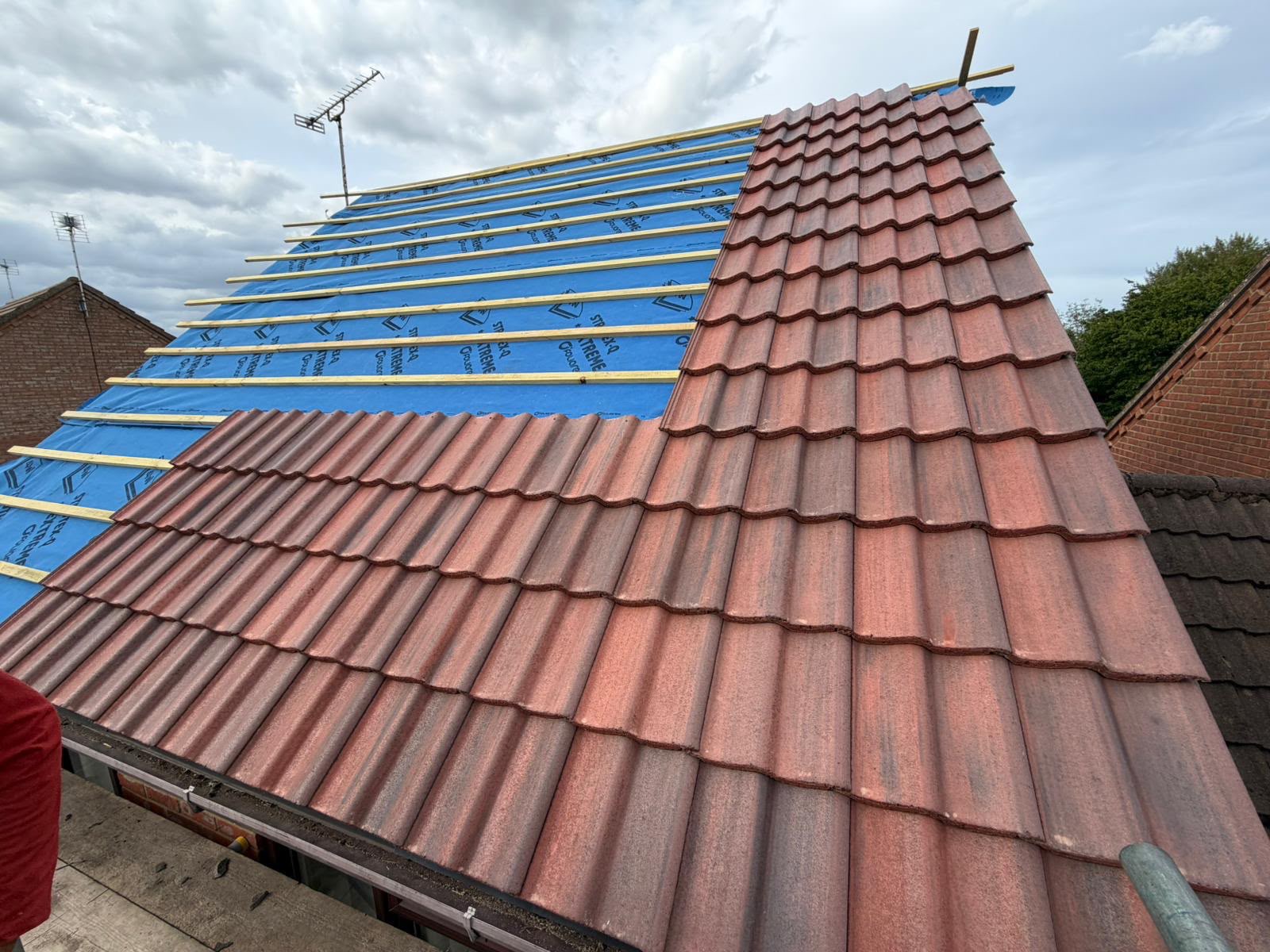 Red roof tiles being laid over blue underlay